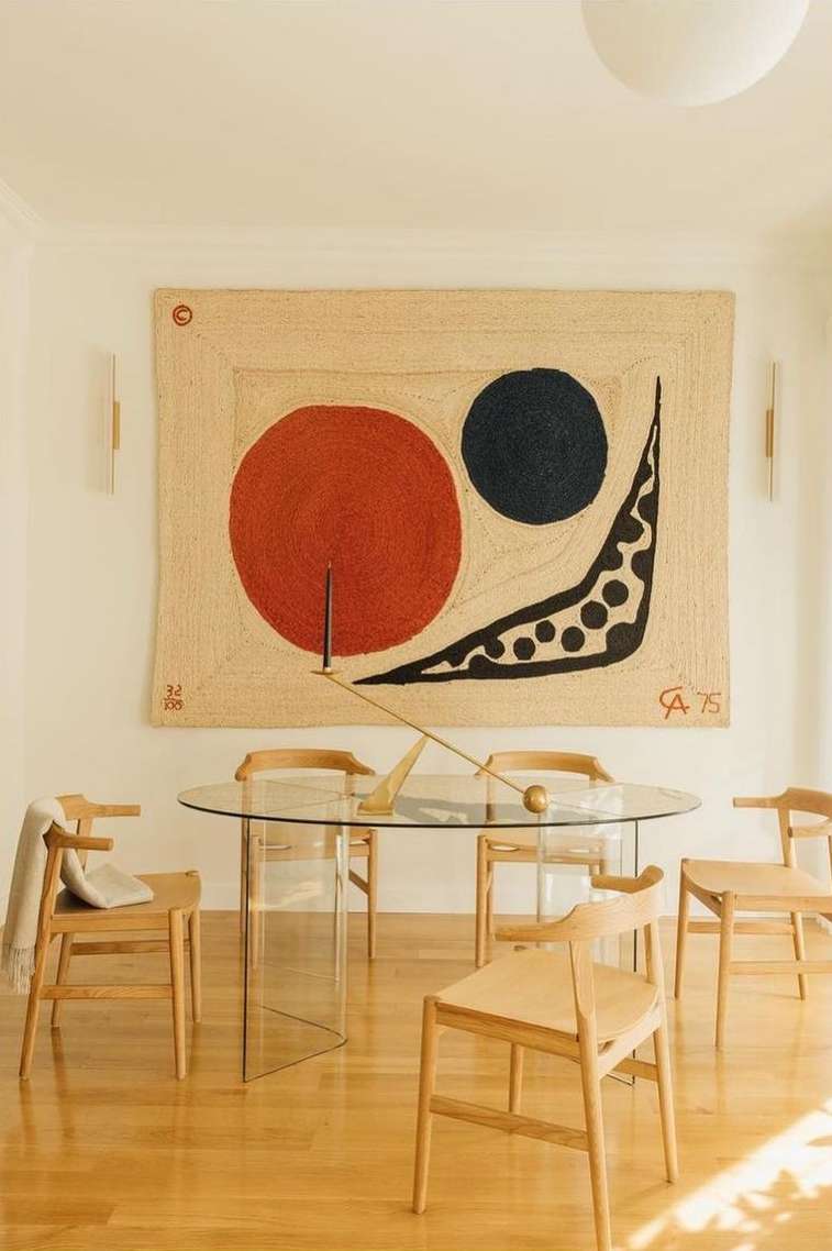 Dining room features an oval glass table surrounded by six light wood chairs, lit by modern sconces, and decorated with abstract art.