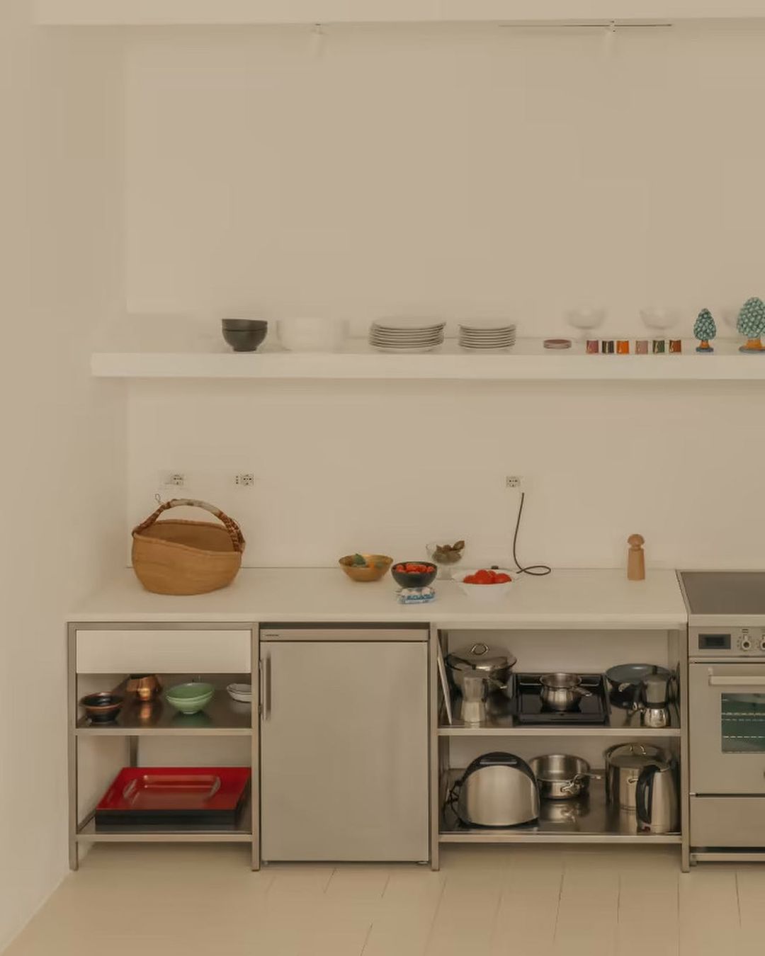Bright, minimalist kitchen interior featuring white walls, shelves stocked with dishware, and an assortment of cooking utensils and appliances.