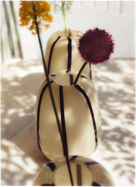 Arrangement of three cream-colored vases with black stripes, each holding a different colored flower against a neutral background.
