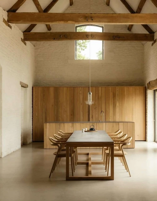 Interior view of a spacious, modern dining room featuring a large wooden table surrounded by wooden chairs, with natural light.