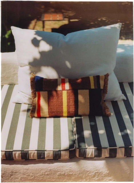 Outdoor seating area with white cushions and a striped seat cushion, topped with a woven decorative pillow in natural light.