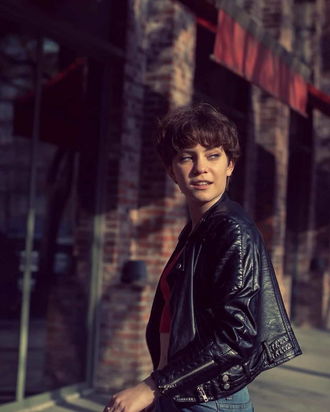 Woman with short brown hair wearing a black leather jacket over a red top on a city street