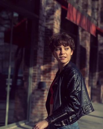 Woman with short brown hair wearing a black leather jacket over a red top on a city street