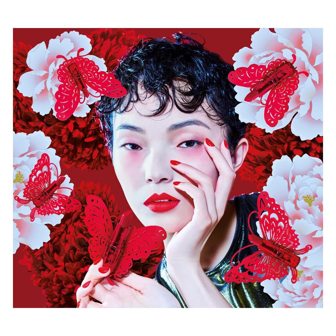 Beauty shot featuring a woman with short black hair, red lipstick and manicure, posing with red butterfly hair clips and peonies.