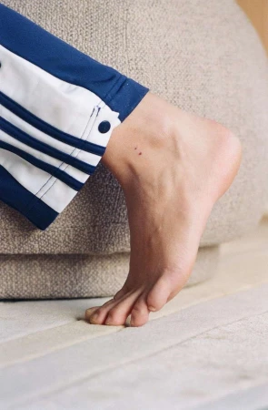 Close-up of a person's foot in blue track pants with white stripes, resting on a beige upholstered surface.