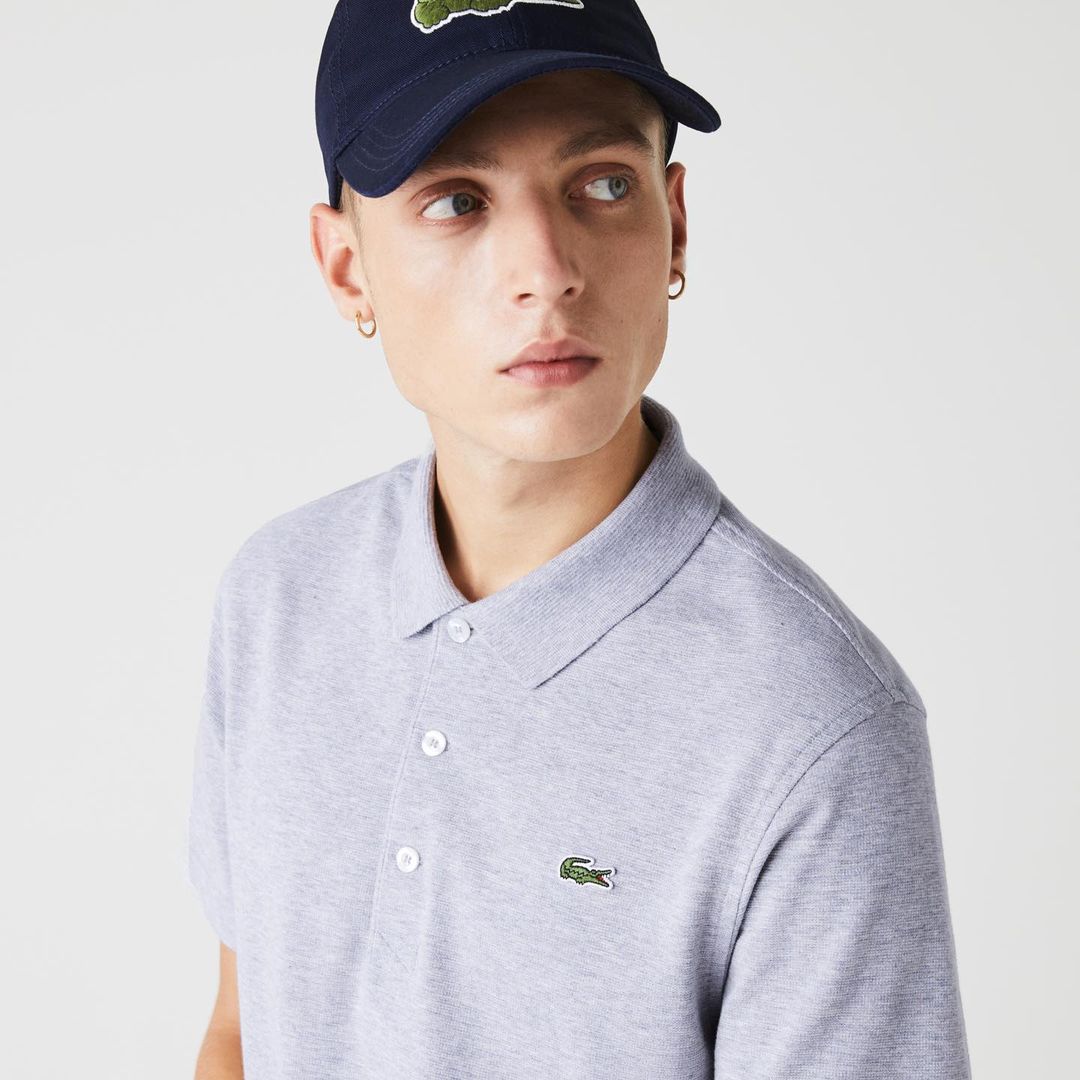 A young adult male is pictured wearing a grey polo shirt and a navy baseball cap, posing in a studio setting with a neutral backdrop.