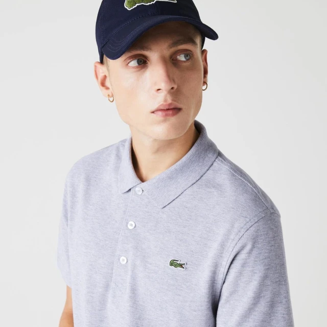 A young adult male is pictured wearing a grey polo shirt and a navy baseball cap, posing in a studio setting with a neutral backdrop.