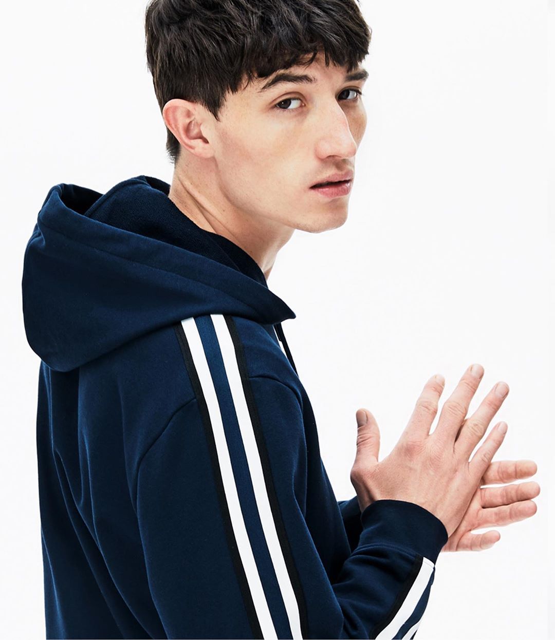 Close-up shot of a young adult man looking over his shoulder wearing a blue hooded sweatshirt with white stripes in a bright photo studio.