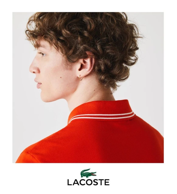Profile of a curly-haired male model in a red polo shirt with white accents, isolated on a clean, bright white background. Fashion shot.