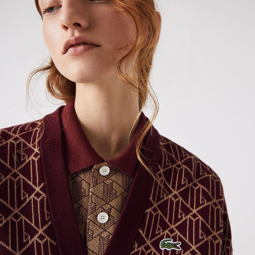 Close-up studio shot of a person wearing a burgundy patterned cardigan and a matching polo shirt. Lacoste logo visible on cardigan.
