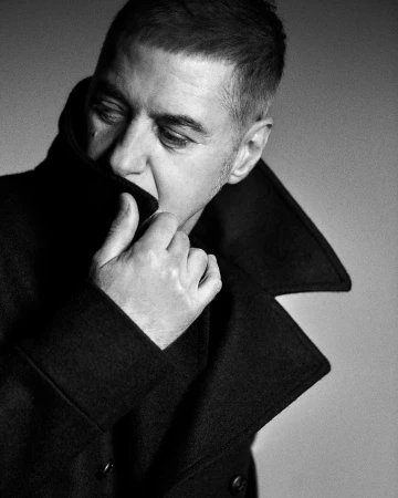 Monochrome portrait of a man pulling up the high collar of his dark wool coat, photographed in Paris.