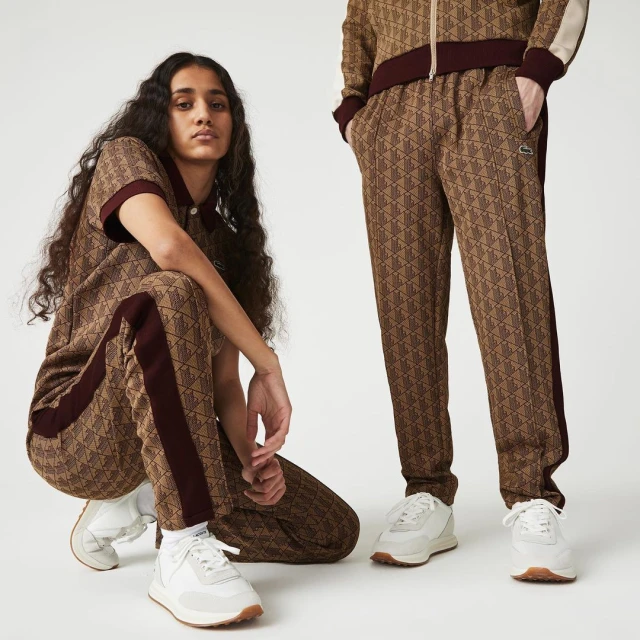 Two people wearing patterned Lacoste tracksuits and white sneakers in a studio setting, showcasing fashion apparel and sporty style.
