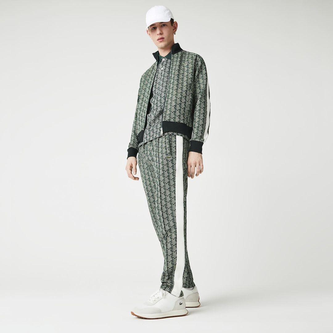 Model in patterned green tracksuit and white cap standing against a white backdrop