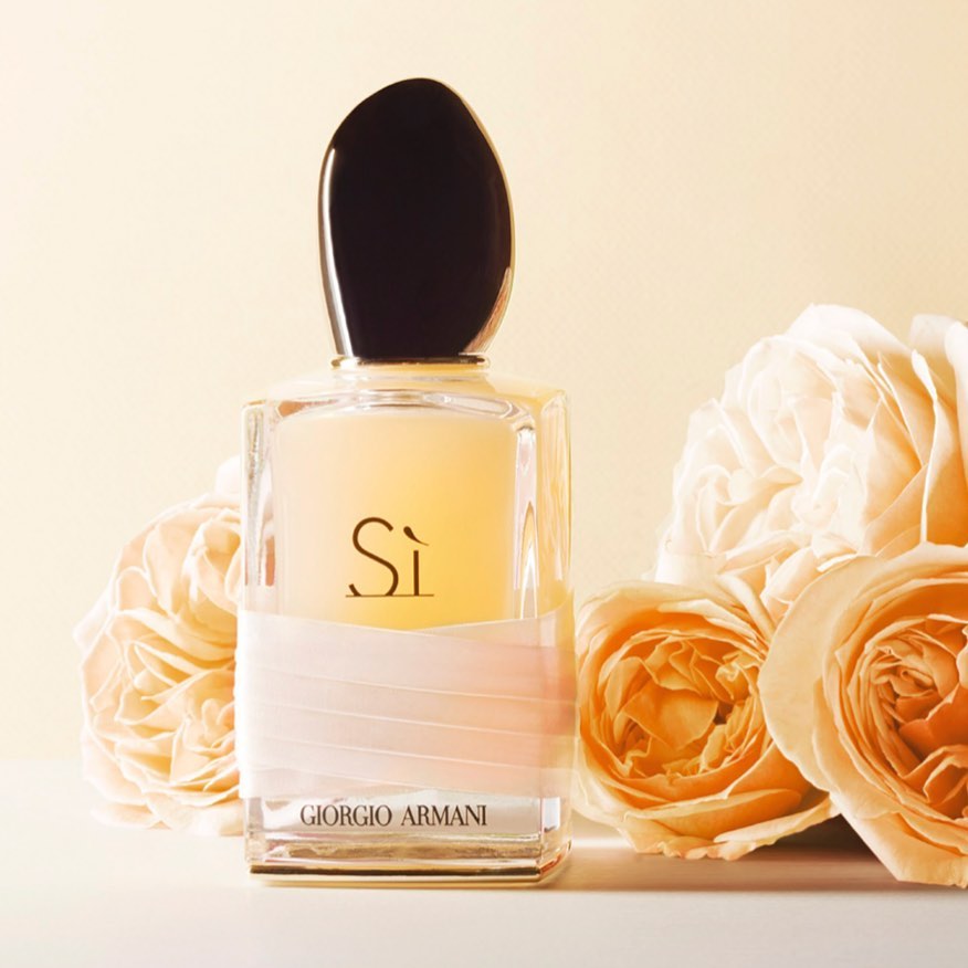 Giorgio Armani perfume bottle with pale peach ribbon surrounded by soft peach-coloured roses on a light background