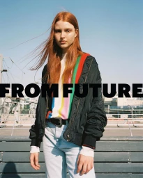 Red-haired female model wearing black bomber jacket and striped sweater standing outdoors in Paris by Max Vigato