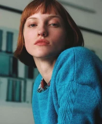 Portrait of a woman with red hair wearing a vibrant blue knitted sweater and patterned shirt collar, photographed by Max Vigato.