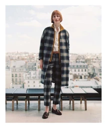 Model standing on a rooftop in Paris wearing a plaid coat, matching trousers, white shirt, and loafers.