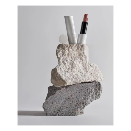 Cosmetic product photography featuring lipstick tube and white container balanced on rough stone, showcasing beauty and textures.