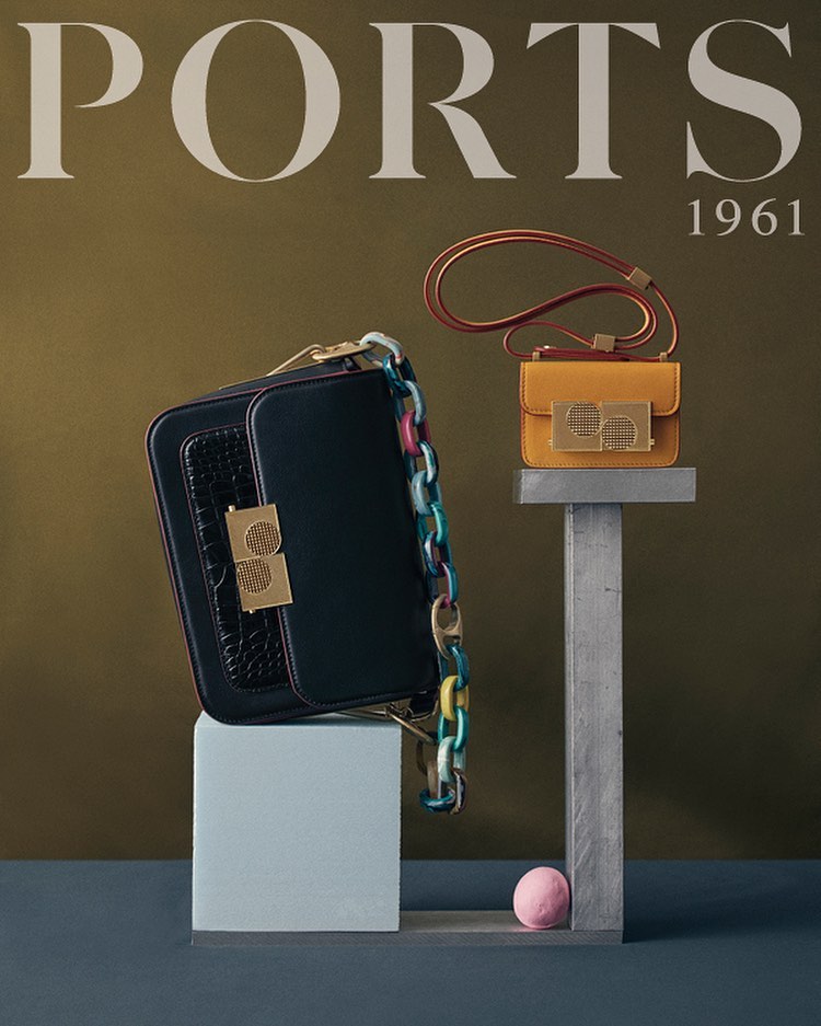 Fashion still life featuring two designer handbags on geometric stands. A black chain-strap bag and a small yellow purse.