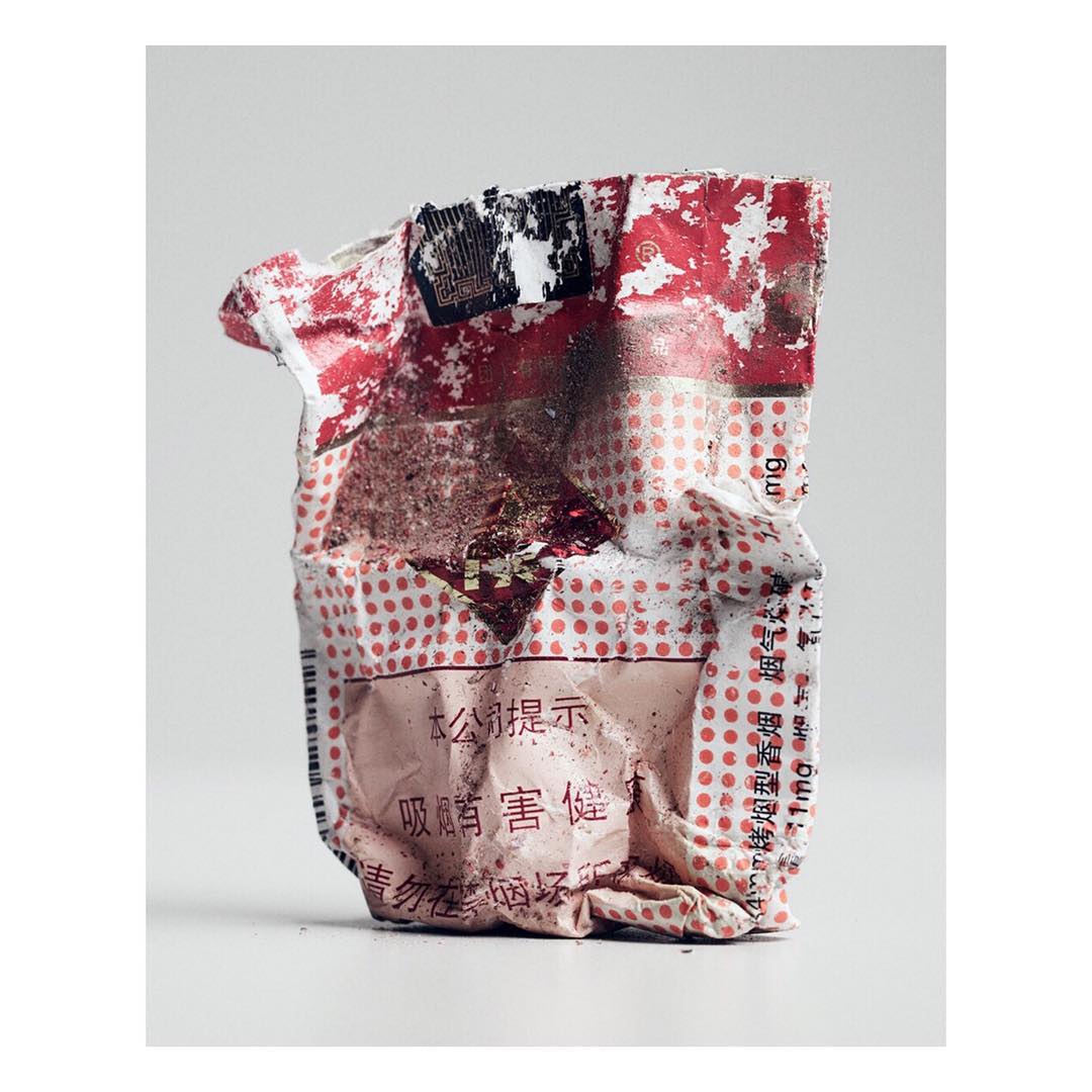 Crushed and crumpled beverage container with red and white polka dots and Chinese text on a white surface against a grey background.