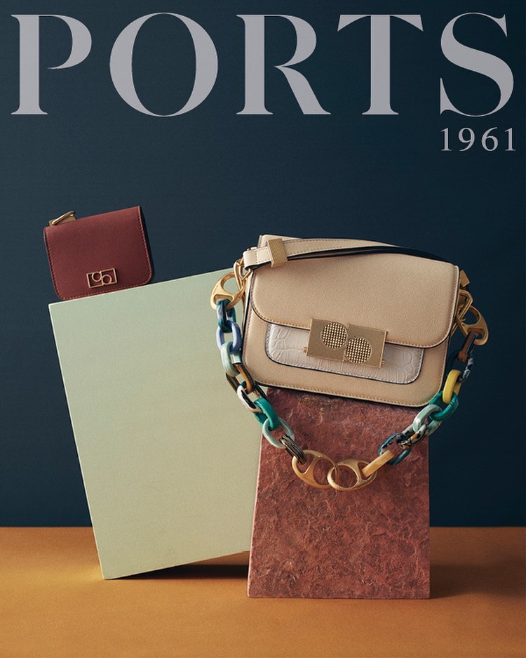 Ports 1961 brand handbag and purse on geometric pedestals against a blue backdrop, showcasing fashion accessories and brand identity.
