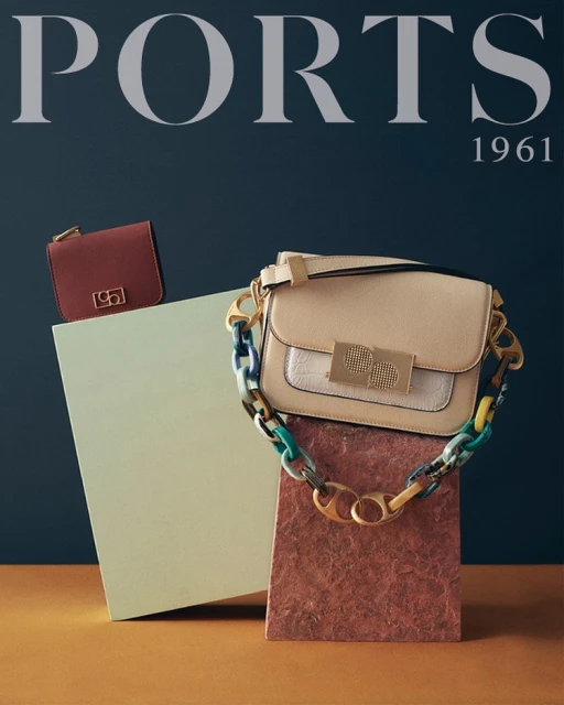 Ports 1961 brand handbag and purse on geometric pedestals against a blue backdrop, showcasing fashion accessories and brand identity.
