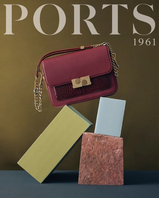 Burgundy leather handbag with gold chain strap, poised above geometric blocks in olive, blue and terra-cotta, against a brown backdrop.