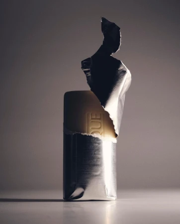 Wrapped bar with silver foil packaging illuminated in studio setting, casting soft shadows on a light surface against a grey background.