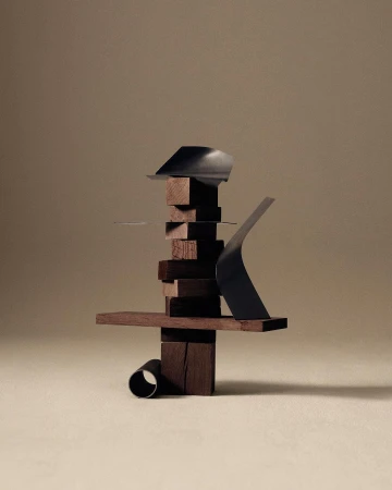 Abstract sculptural composition with dark brown stacked wooden blocks and dark metallic elements on a tan background in studio lighting.
