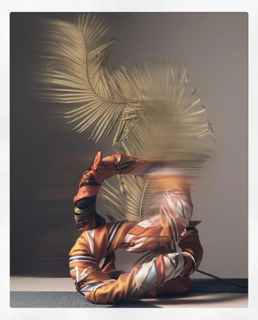 Artistic photo of an orange jacket shaped into a circle with palm fronds, creating an abstract fashion and nature fusion on a gradient background.