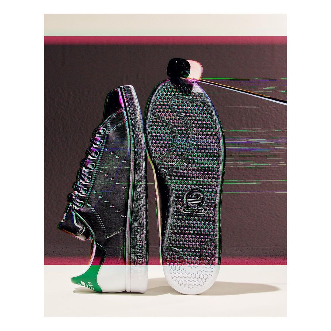 Studio shot of a pair of Adidas Stan Smith black leather sneakers with white soles featuring glitch effects and graphic accents.