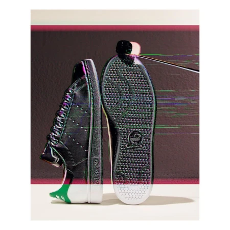 Studio shot of a pair of Adidas Stan Smith black leather sneakers with white soles featuring glitch effects and graphic accents.