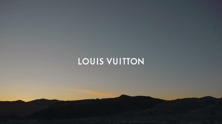 Mountains silhouette and the Louis Vuitton brand text logo in a commercial outdoor shot, during golden hour lighting, for a fashion campaign.