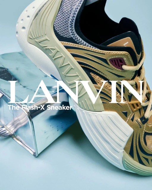 Close-up of a gold and black Lanvin Flash-X sneaker propped on a metallic cube against a light blue background, showcasing its design.