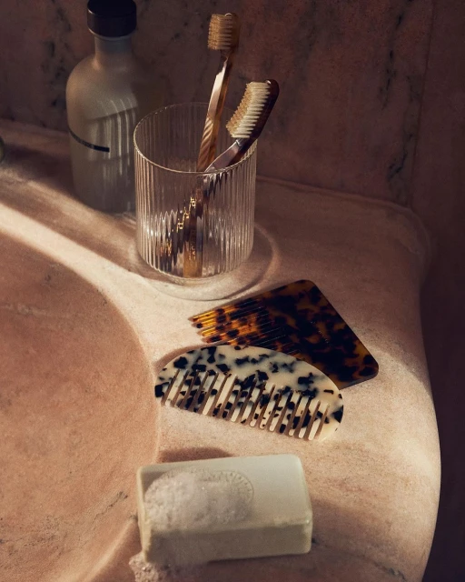 Still life in bathroom with tortoise shell combs, toothbrushes in glass, and a bar of soap, capturing a minimalist aesthetic.