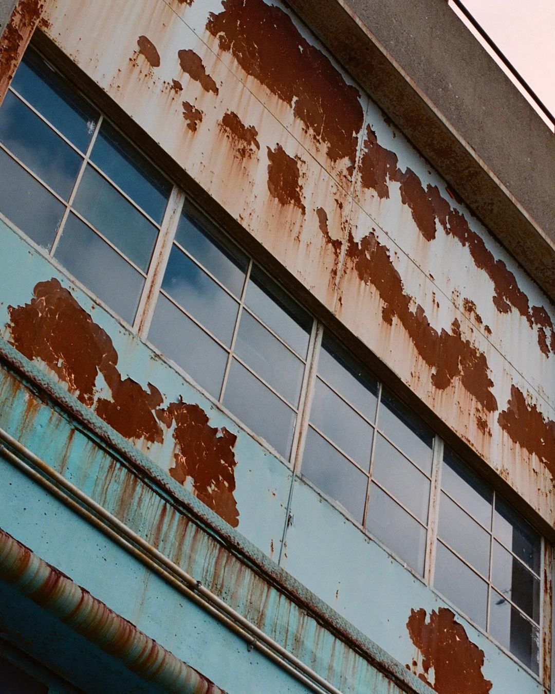 Exterior view of an industrial building featuring rusted metal cladding, a row of windows, and the architectural design of the structure.