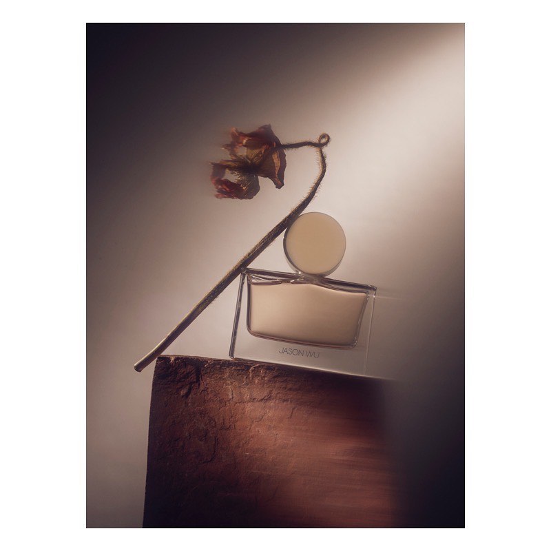Still life shot of Jason Wu perfume bottle with dried floral elements against a diffused background with muted, earth-toned colors.