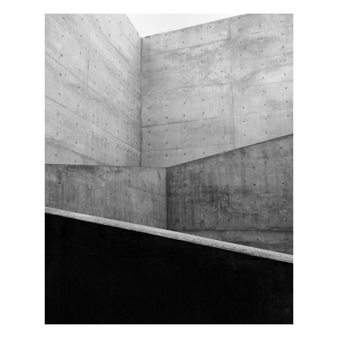 Black and white architectural image showcasing raw concrete walls in an indoor setting, emphasizing geometric shapes and textures.