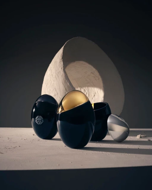 Four black and silver cosmetic containers with an ovoid shape are arranged on a cream surface, with a large, textured semi-circle in the backdrop.