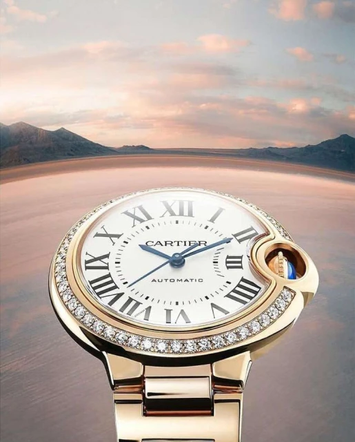 Close-up of a gold Cartier watch with a diamond bezel on a blurred background of a salt flat and distant mountains at sunset.