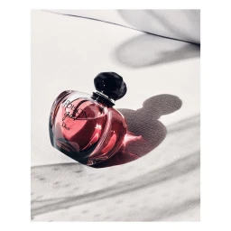 Round glass perfume bottle with dark cap resting on a white surface, casting a soft shadow with gentle highlights.