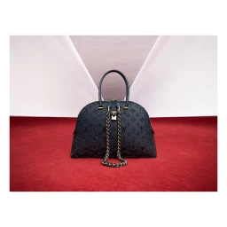 Black embossed monogram handbag resting on a red textured surface with a geometric background, photographed by Maxime Poiblanc.