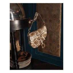 Snakeskin print designer saddle handbag hanging from a metallic stand in a luxurious interior setting.