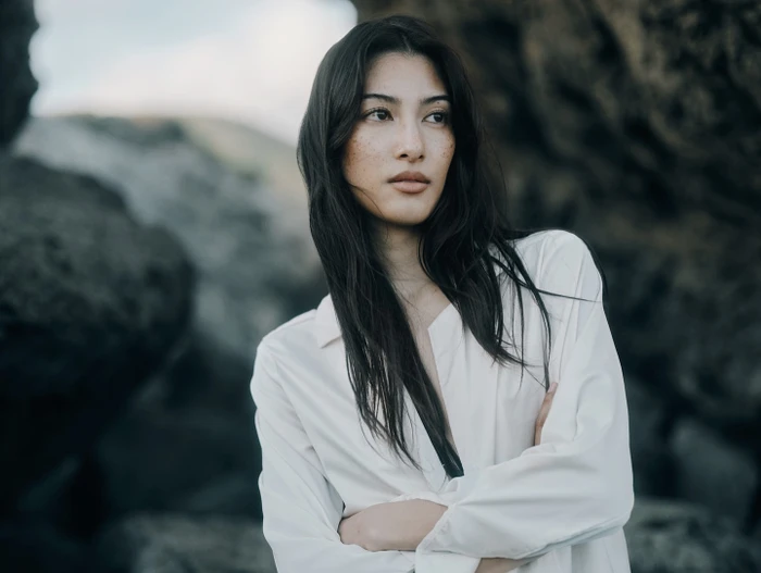 Portrait of a woman with dark hair and freckles wearing a white collared shirt against rocky outdoor background
