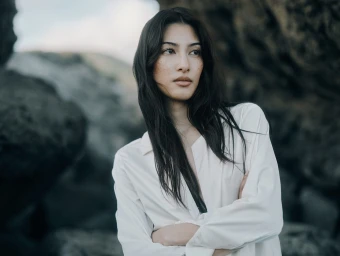 Portrait of a woman with dark hair and freckles wearing a white collared shirt against rocky outdoor background