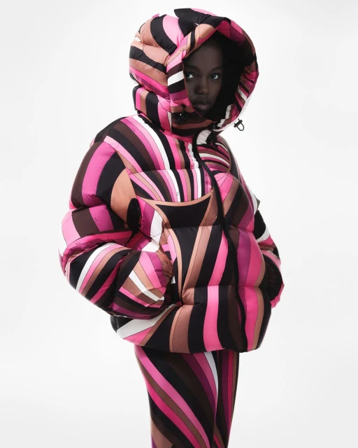 Adult woman in a hooded puffer jacket and leggings with a bold, colorful swirling pattern against a clean, bright white backdrop.