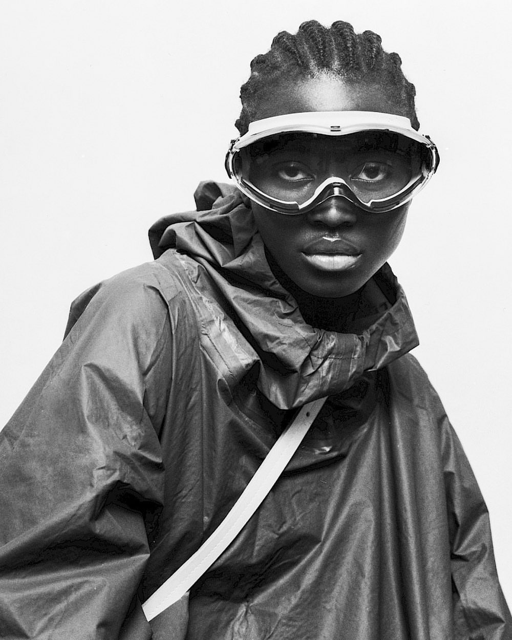 A model wears a hooded raincoat and visor goggles against a white backdrop in a portrait showcasing a futuristic and utilitarian style.