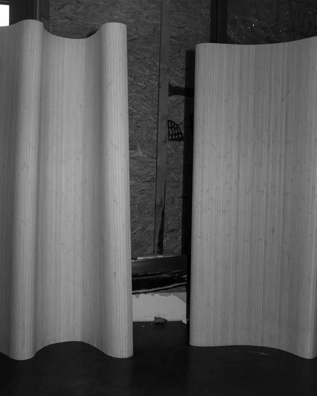 Monochrome shot of two light-toned wooden panels, one curved, set indoors against a textured wall, exhibiting simple elegance.