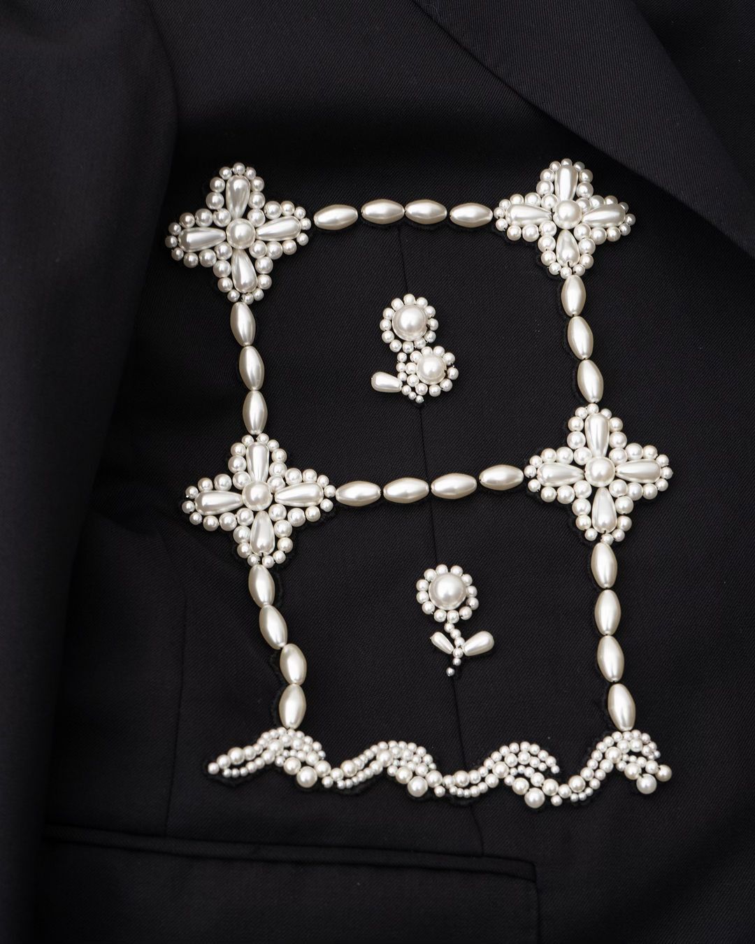 Elegant black blazer featuring unique pearl embellishments forming a square and floral designs, creating a sophisticated fashion statement.