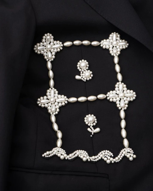 Elegant black blazer featuring unique pearl embellishments forming a square and floral designs, creating a sophisticated fashion statement.
